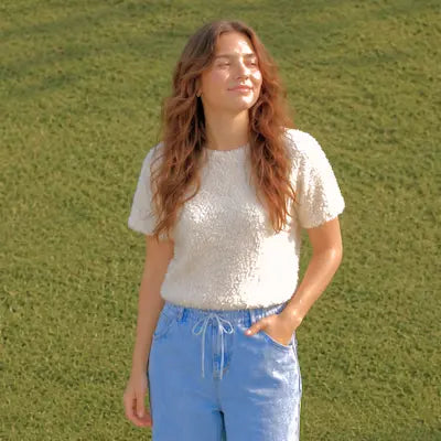 Woman wearing a white textured top and blue jeans standing in a grassy field