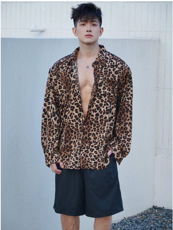 Man wearing a leopard print shirt and black shorts against a light blue wall.