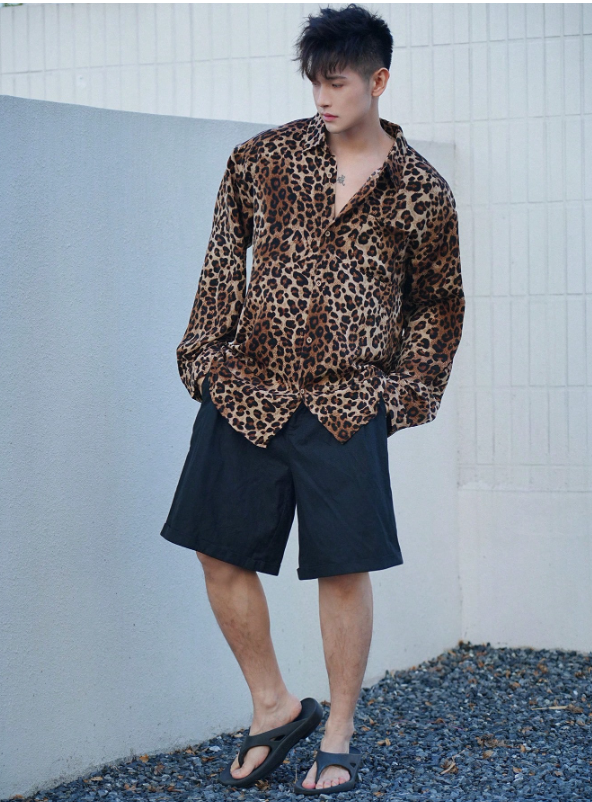 Person wearing a leopard print shirt and black shorts against a tiled wall.