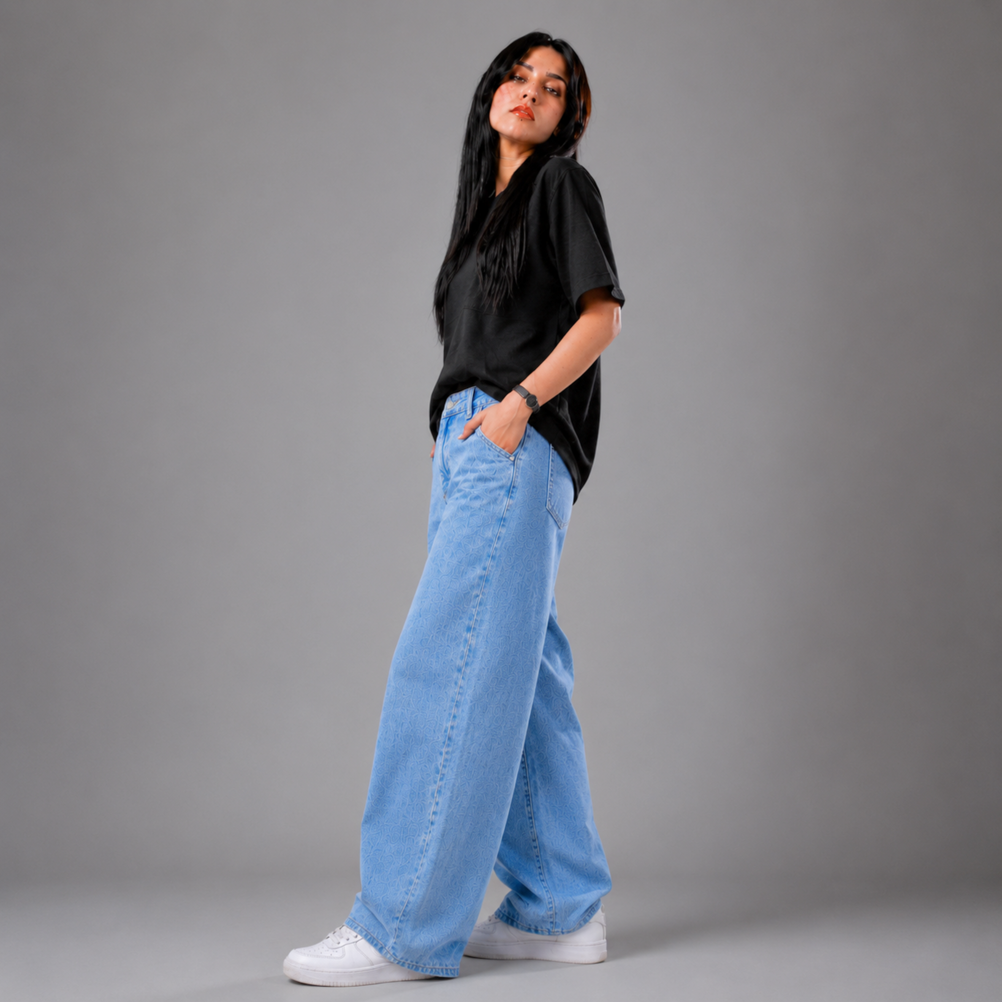 Women's light wash wide leg denim jeans with a relaxed baggy fit, high-rise waist, and soft lightweight fabric, styled with a black oversized t-shirt and white sneakers in a studio fashion photoshoot.
