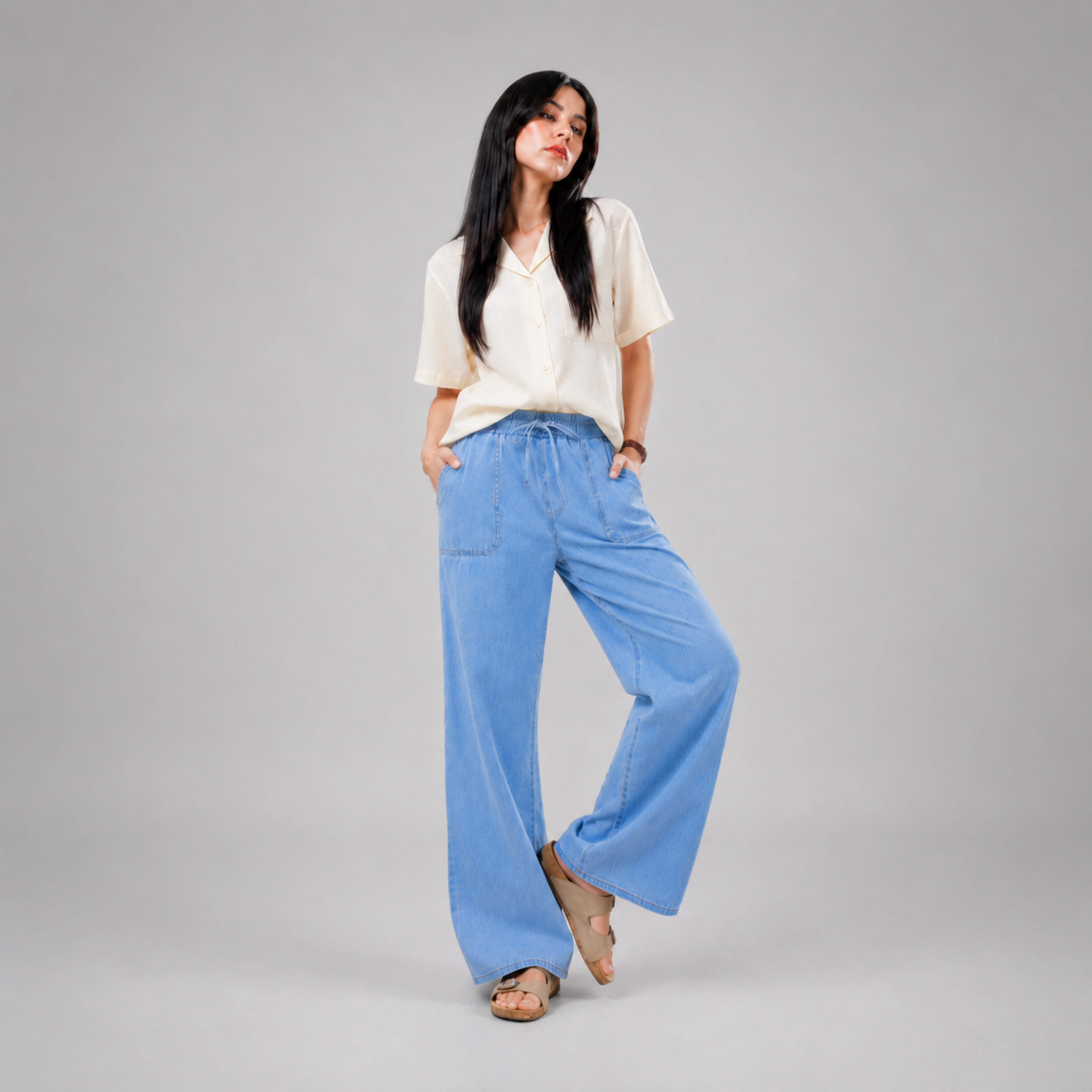 Women's light wash wide leg denim jeans with elastic drawstring waist, relaxed baggy fit, front patch pockets, and lightweight comfortable fabric, modeled in a casual fashion studio setting by Khaazi.