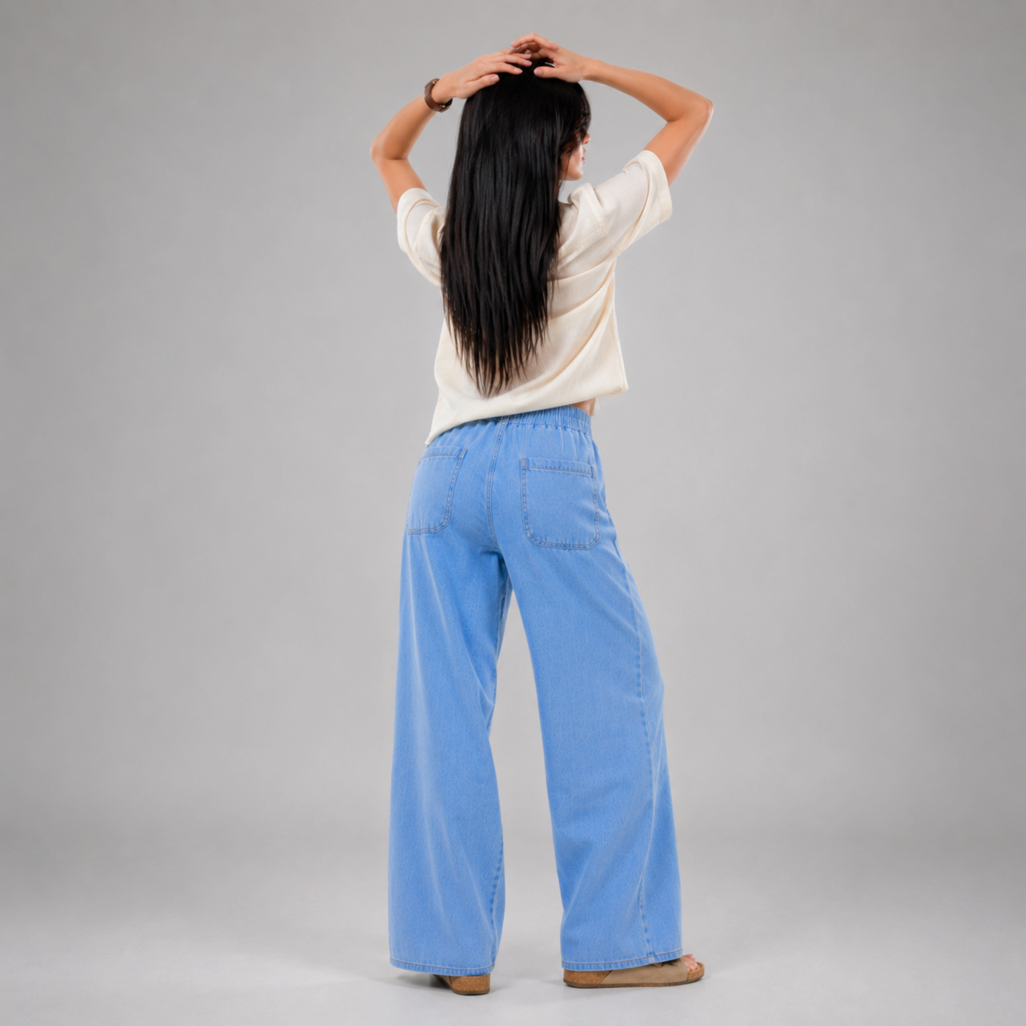 Women's light wash wide leg denim jeans with elastic drawstring waist, relaxed baggy fit, front patch pockets, and lightweight comfortable fabric, modeled in a casual fashion studio setting by Khaazi.
