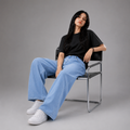 Women's light wash wide leg denim jeans with a relaxed baggy fit, high-rise waist, and soft lightweight fabric, styled with a black oversized t-shirt and white sneakers in a studio fashion photoshoot.