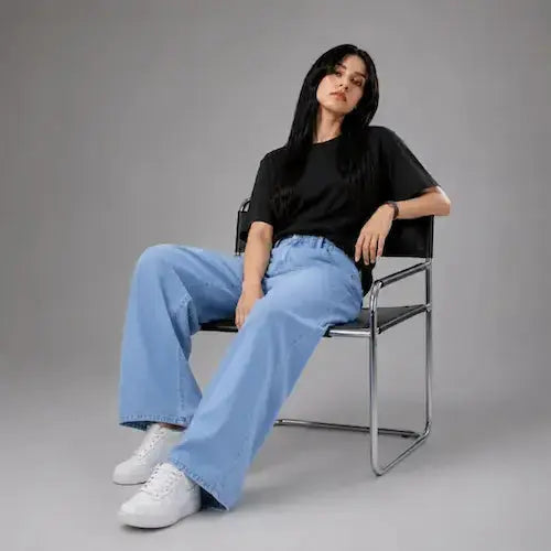 Model sitting on chair wearing wide-leg blue denim jeans—KHAAZI
